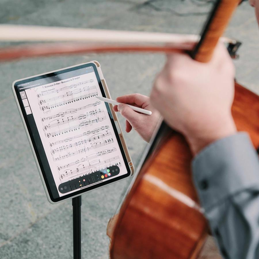 Cello neben einem Tablet mit digitalen Noten; eine Hand hält einen Stift am Bildschirm.